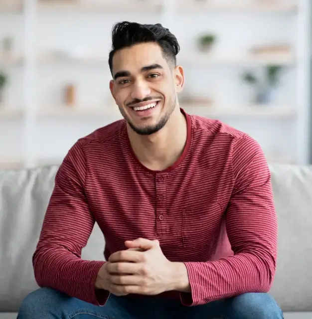 Smiling man in burgundy striped shirt sitting on couch for restorative dentistry services in Sugar Land.