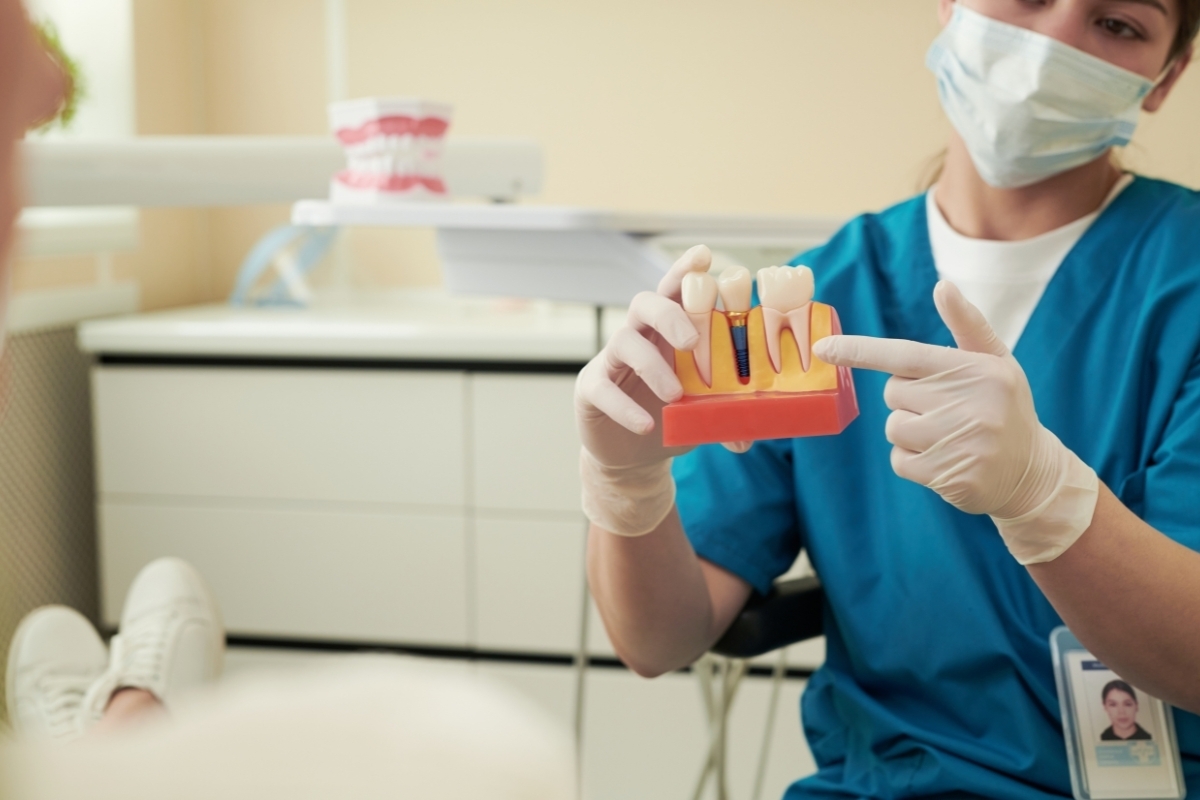Dental professional demonstrating dental implant model with artificial teeth to patient in treatment room.
